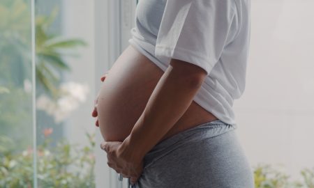 Young Asian Pregnant woman holding her belly talking with her child. Mom feeling happy smiling positive and peaceful while take care baby, pregnancy near window in living room at home concept.