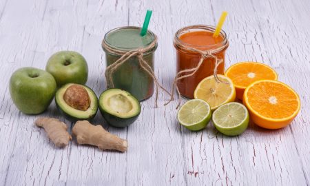 green and orange detox coctails stands on white table with fruit