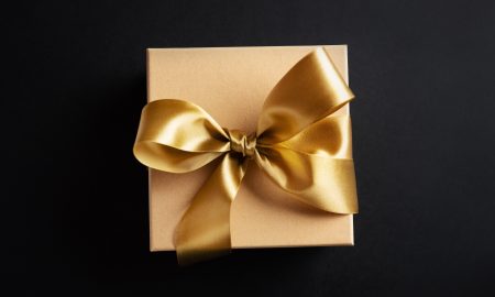 Cute gift box with golden ribbon bow on dark background. Flat Lay.