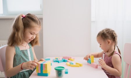 Lovely kids plaing with colorful wodden blocks in a creative educational game as they stand at a pink table