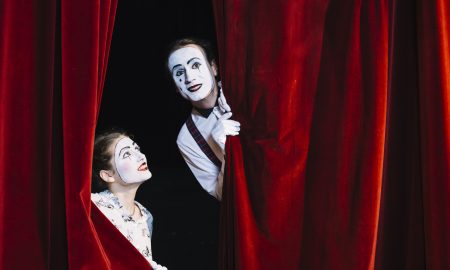 smiling-female-mime-artist-looking-at-male-mime-artist-peeking-from-curtain