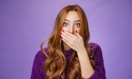 Impressed speechless cute ginger girl hearing stunning gossip covering mouth form amazement and shook raising eyebrows wondered as reacting to unexpected revelation or rumor over purple background
