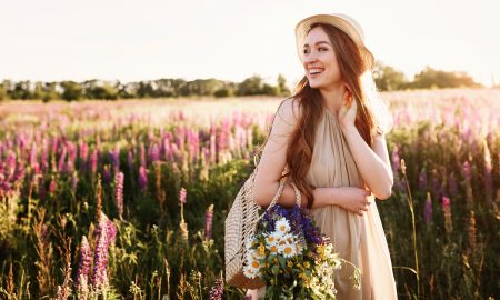 Happy young girl walking in flower field at sunset. Wearing straw hat and bag full of flowers. Horizontal copy space portrait.