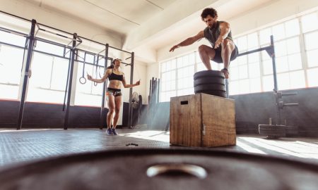 Fit young man box jumping with woman exercising with skipping ropes at a cross training style gym. Couple during intense workout session at health club.