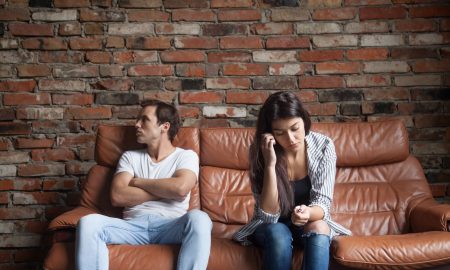 Frustrated upset couple in quarrel not talking after fight, offended stubborn insulted jealous man sitting silent on sofa at home with sad depressed disappointed woman, marriage relationships problem