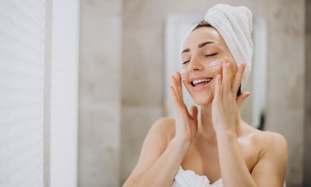 Young woman applying face cream on her face with towel on head